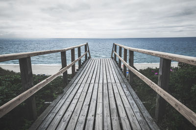 Wooden bridge over roses bushes towards beach and north sea water, on sylt island, germany.