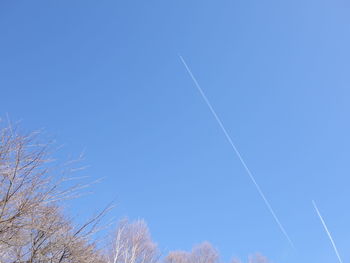 Low angle view of vapor trails against clear blue sky