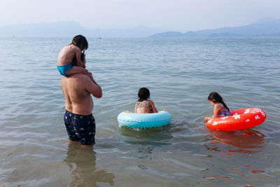 Rear view of father with three children getting inside the water with floating rings