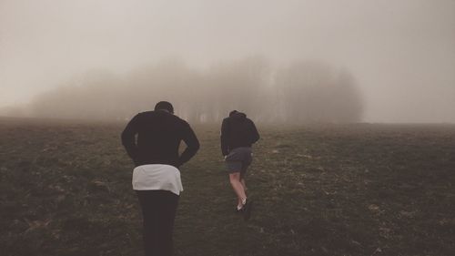 Rear view of people walking on landscape against sky during foggy weather