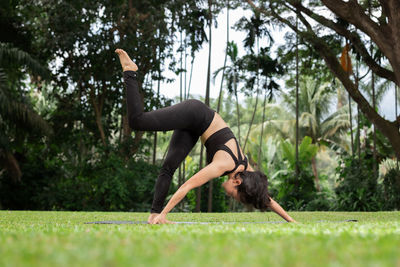 Full length of woman exercising on grassy land against trees