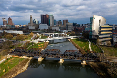 Bridge over river amidst buildings in city against sky