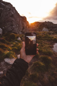 Hand holding smartphone with image of scene backlit by sunset