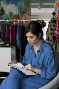 Female owner reading book while sitting in clothing store