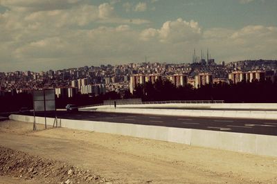 Road by buildings in city against sky