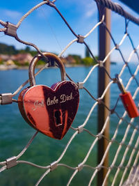 Close-up of love lock hanging from fence against river