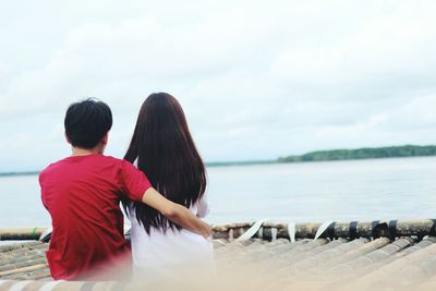 Rear view of man and woman sitting on pier against lake