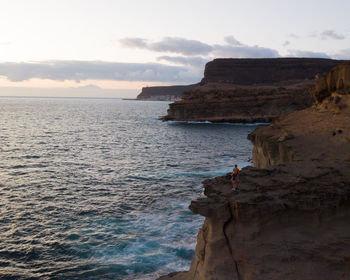 Couple standing on rock formation by sea during sunset