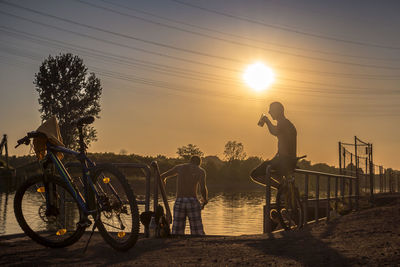 Silhouette people riding bicycle against sky during sunset