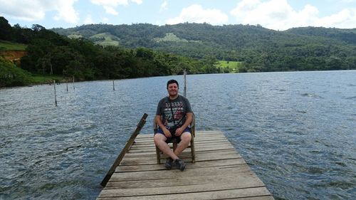 Full length of man sitting on jetty over lake against mountains