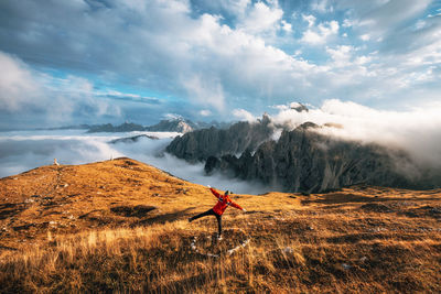 Rear view of mid adult man with arms outstretched standing on mountain against cloudy sky