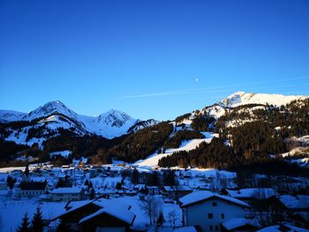 Houses on snowcapped mountain against clear blue sky