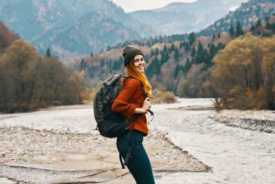 Full length of smiling woman standing in snow covered mountains