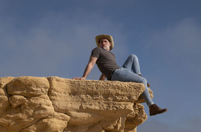 Adult man in cowboy hat sitting on cliff against sky. almeria, spain