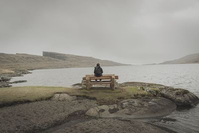 Man sitting on rock by sea against sky