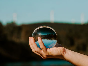 Cropped hand holding crystal ball against sky