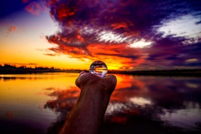 Man holding crystal ball at lake during sunset