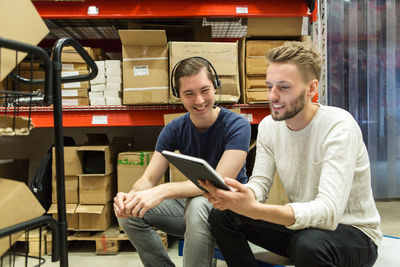 Smiling colleagues discussing over digital tablet while sitting at industry