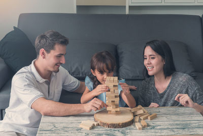 Parents with daughter playing block removal game on table at home