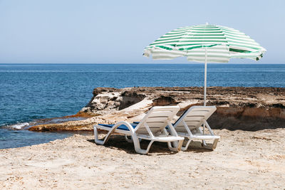 Deck chairs under parasol at beach against clear sky