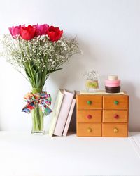 Red tulip flowers in vase by books and drawers on table against wall