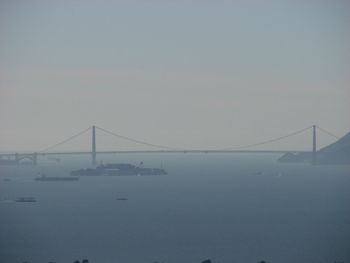 View of suspension bridge over sea against sky during foggy weather