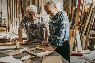 Happy senior craftsmen looking at wooden frames at repair shop