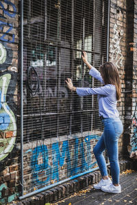 Side view of young woman standing by metal grate