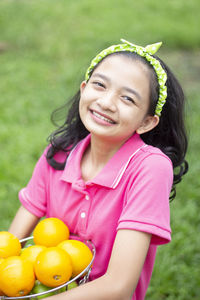 Portrait of happy girl holding oranges in basket while standing on field