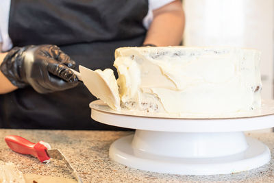 Pastry chef cook confectioner or baker in black gloves and black kitchen apron makes a cake.