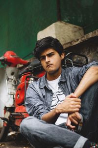 Thoughtful young man looking away while sitting against motor scooter in city