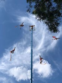 Low angle view of people paragliding against sky