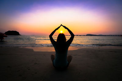 Man relaxing at beach against sky during sunset