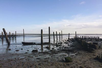 Wooden posts at sea shore against sky