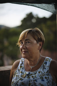 Close-up portrait of senior woman with short hair standing on building terrace during sunset