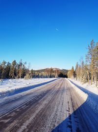 Snow covered road by trees against blue sky