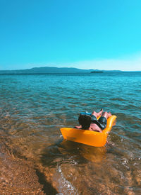 Rear view of man floating on pool raft in lake against sky