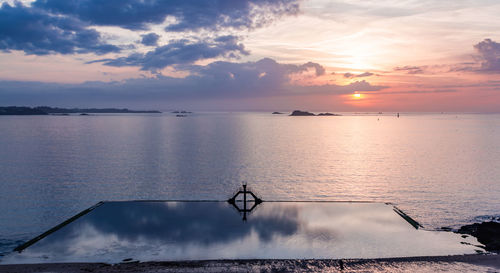 Reflective sea pool against sky at sunset