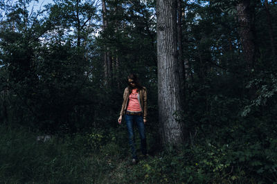 Woman standing by tree trunk in forest