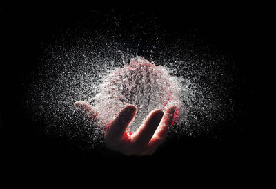 Cropped hand holding water bomb exploding against black background