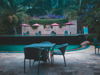 Chairs and tables in swimming pool against trees