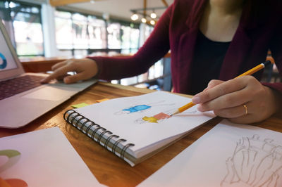 Close-up of fashion designer sketching while working in office
