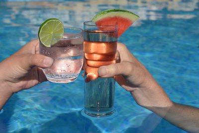 Cropped image of hand holding drink at swimming pool