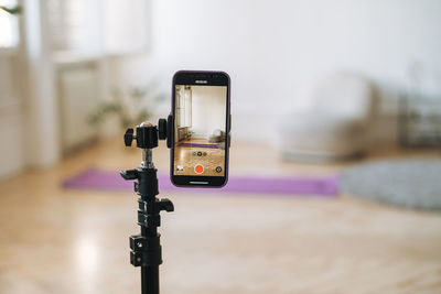 Mobile phone on tripod in empty living room with fitness mats on the floor