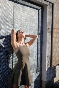 Thoughtful young woman with eyes closed while standing against warehouse