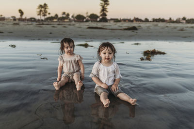 Front view of toddler sisters sitting in water at beach