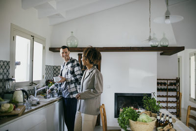 Happy friends talking while standing together in kitchen at home