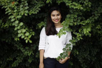 Portrait of smiling young woman standing against plants