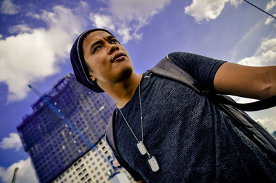 Low angle view of young man standing against sky in city