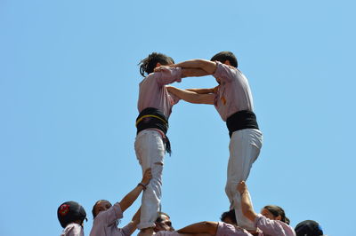 Low angle view of people walking against clear blue sky